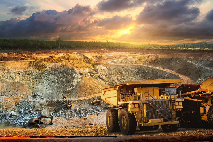 Open-pit mine at sunset with trucks, excavators, and dramatic clouds filling the glowing sky.